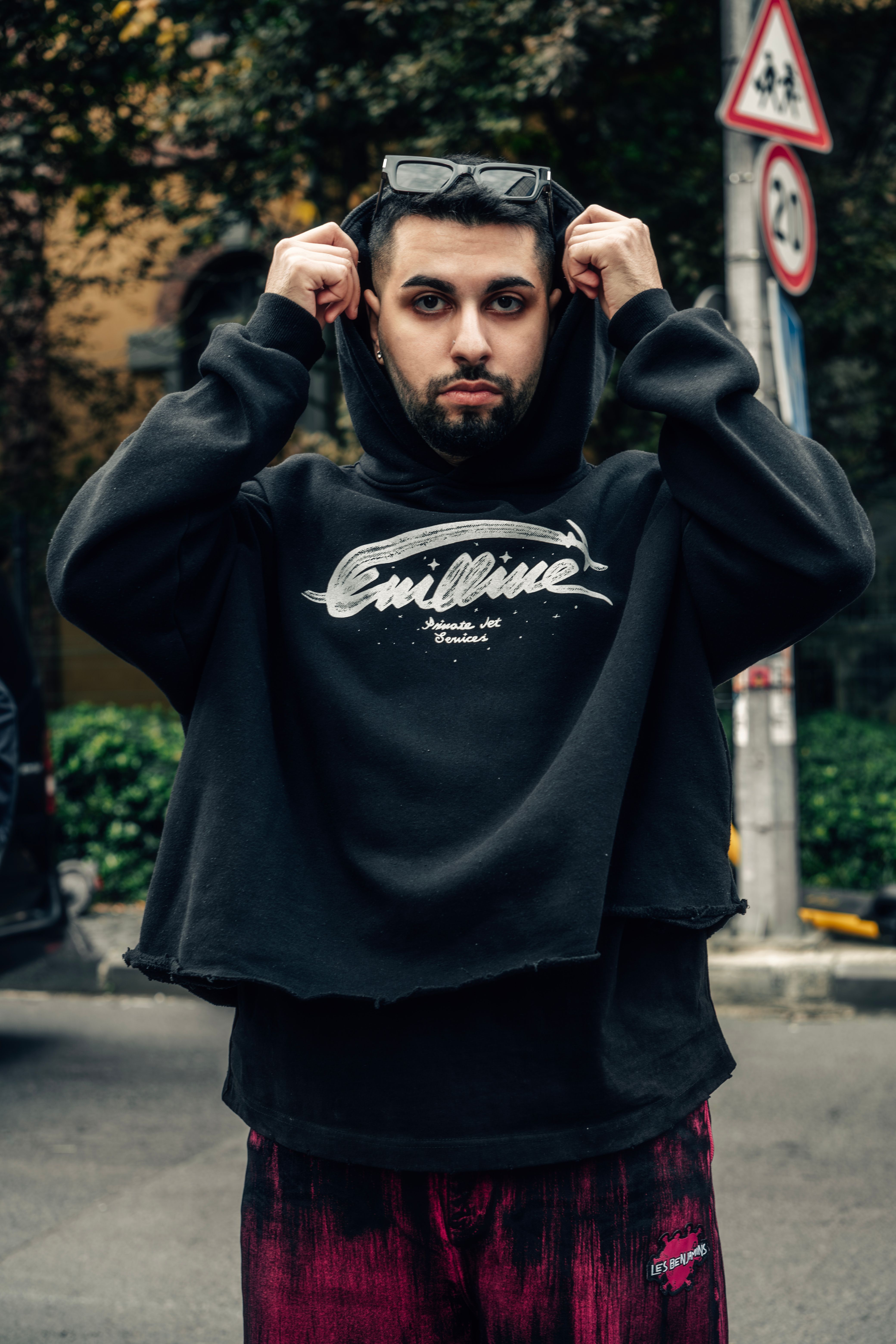 Portrait of a young man adjusting his hoodie in an urban environment.