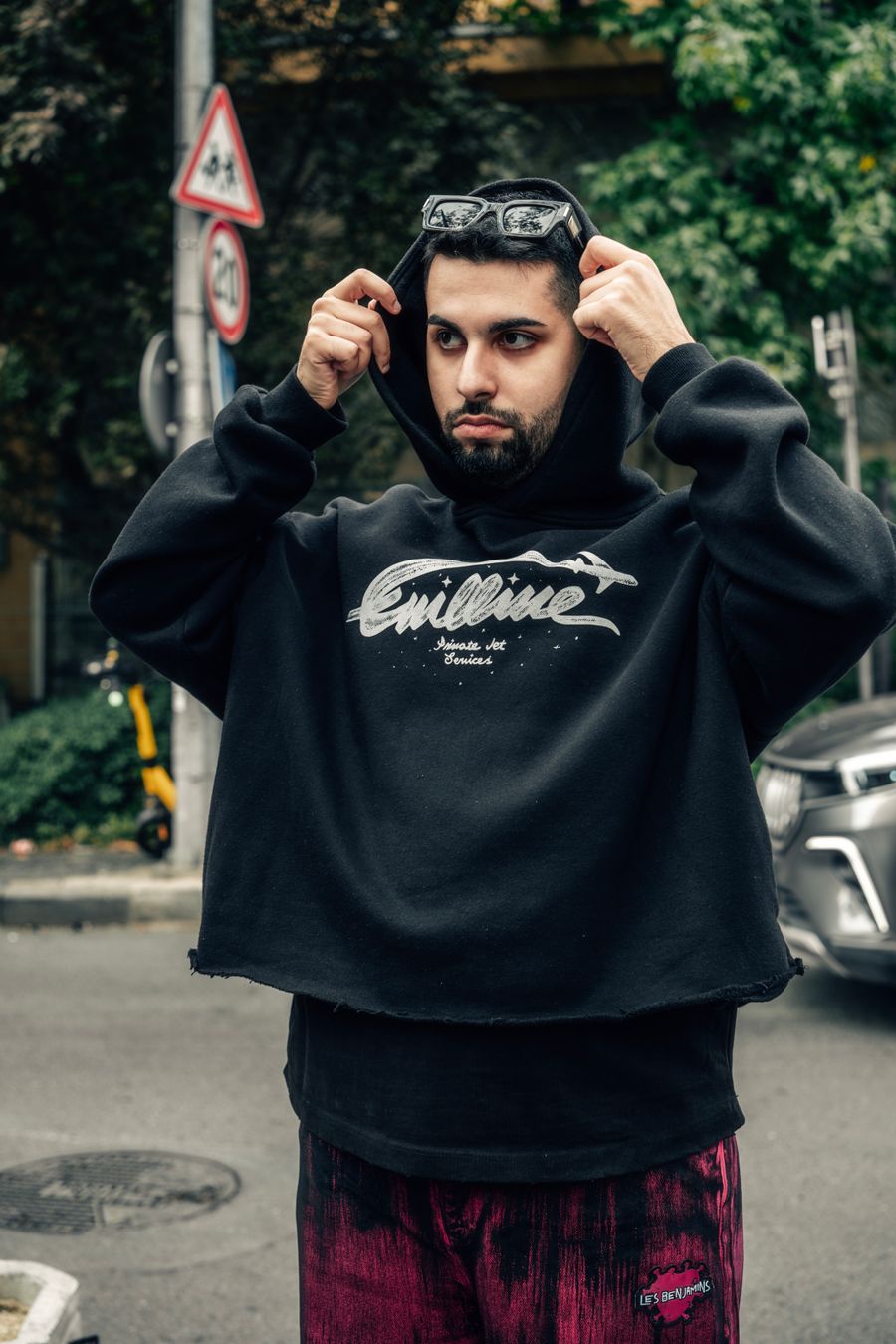 Street style portrait of a man adjusting his hood in a black hoodie on a city street