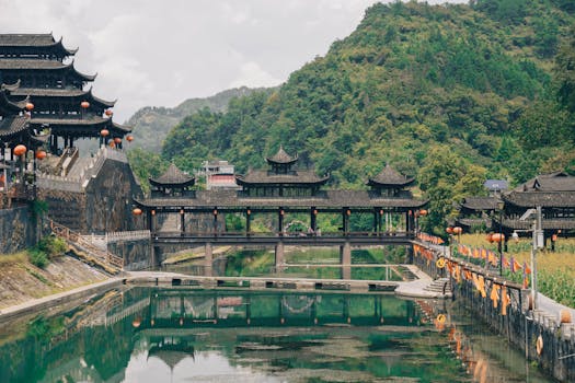 Beautiful traditional Chinese architecture by a tranquil river in a lush mountain setting.