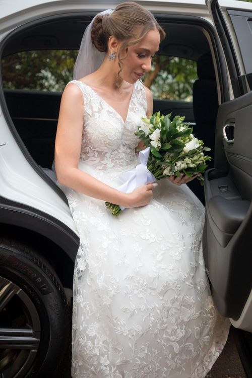 Free Bride in lace dress holding bouquet while entering car, capturing wedding elegance. Stock Photo