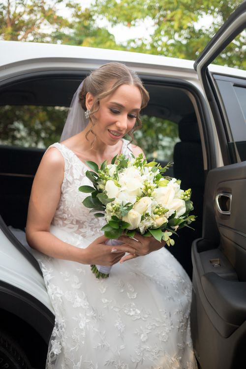 Free A smiling bride in a white dress holding a bouquet as she exits a car. Stock Photo