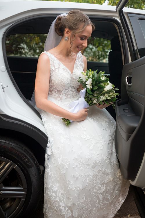 Free Bride in elegant lace gown stepping out of white car holding a bouquet of white flowers. Stock Photo