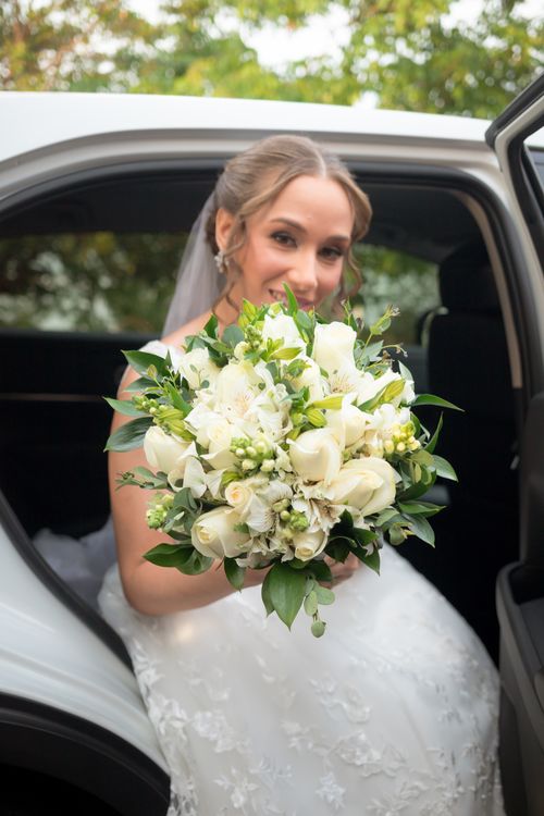 Free Smiling bride in white dress holds bouquet sitting in car, perfect wedding moment. Stock Photo
