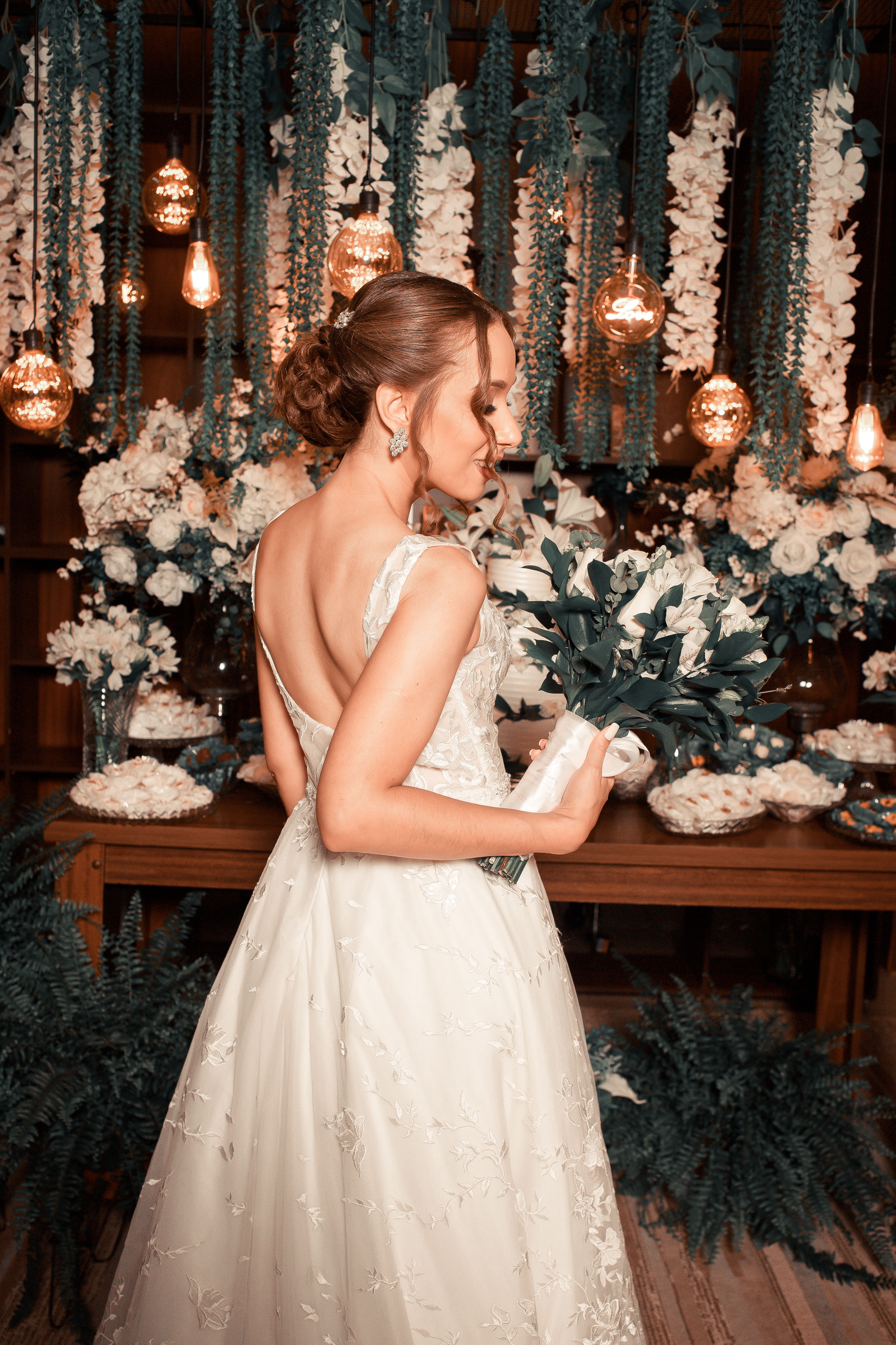 Bride in white gown holding bouquet in a floral decorated setting.