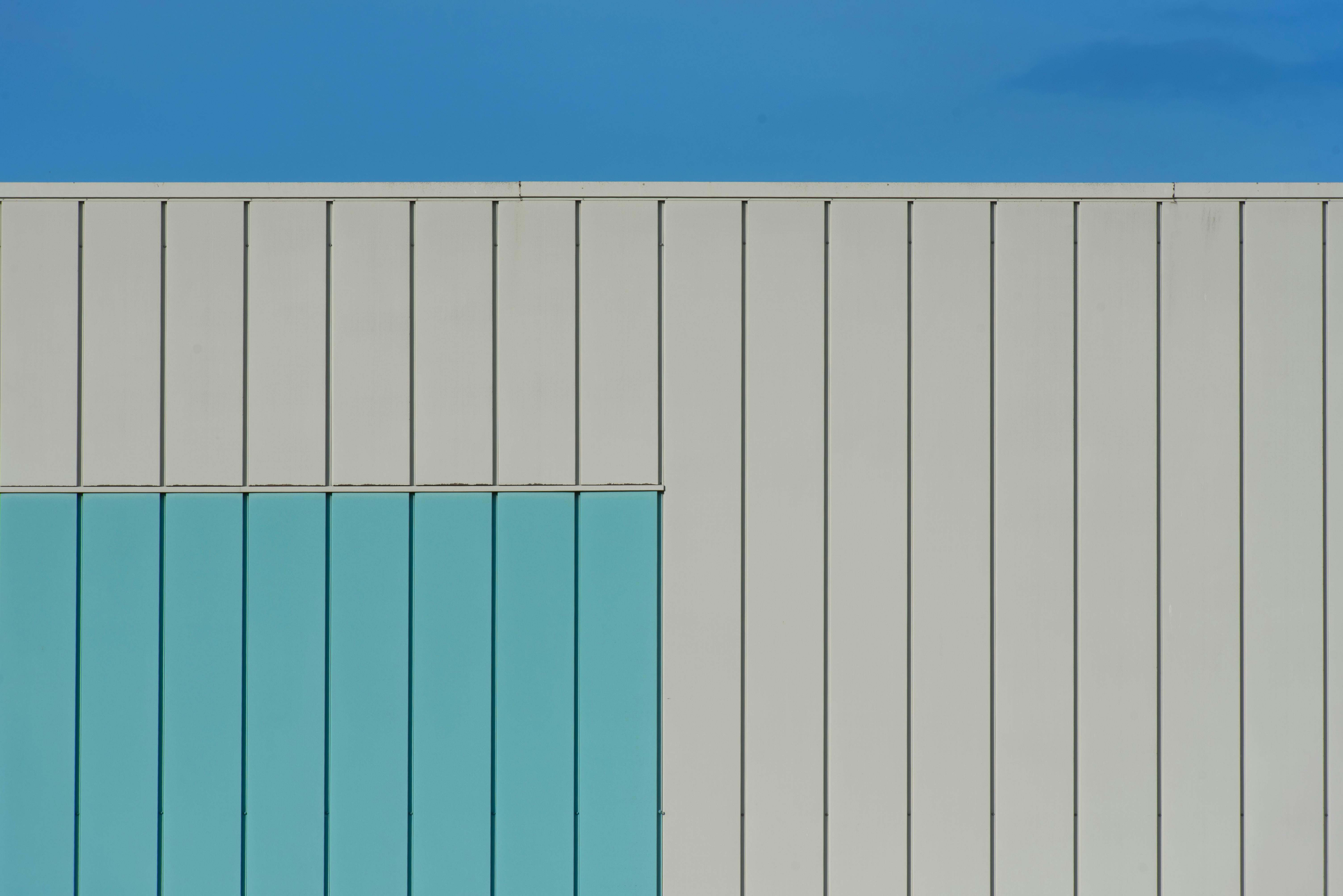 Gratis Vista astratta della facciata di un edificio moderno con design geometrico e accenti blu sotto un cielo limpido. Foto a disposizione