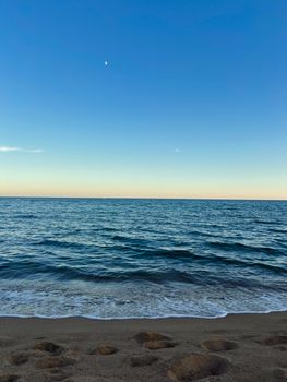 Serene beach scene captured at dusk with a blue sky and visible moon.