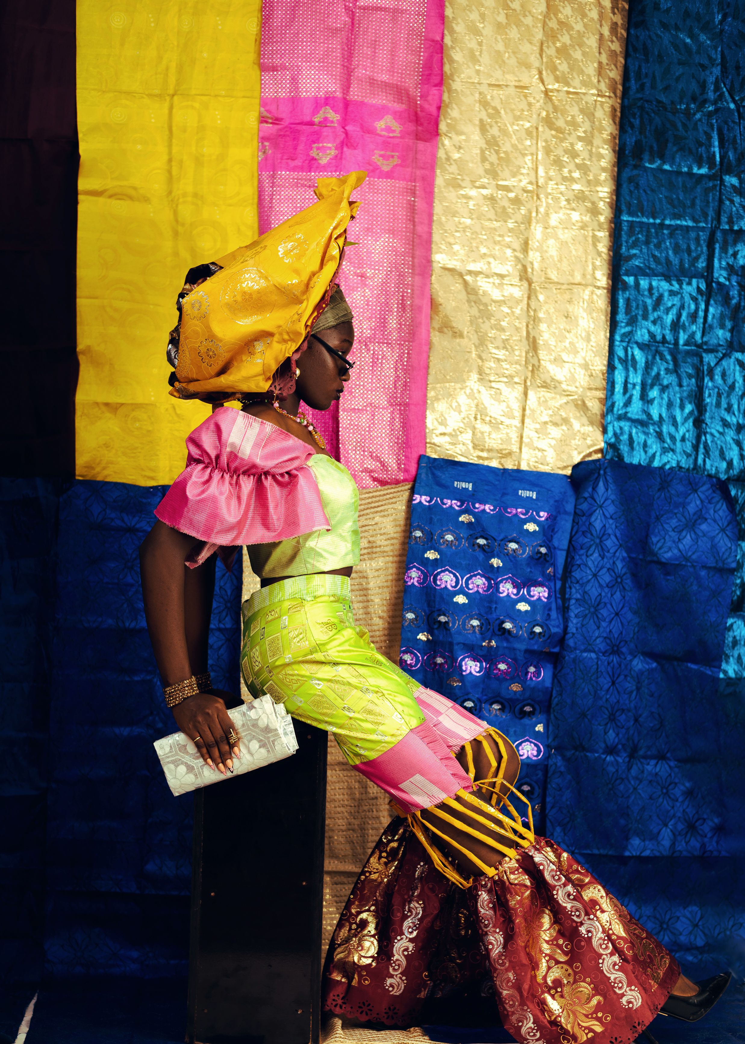 Stylish African woman in colorful attire posing against textile backdrop.
