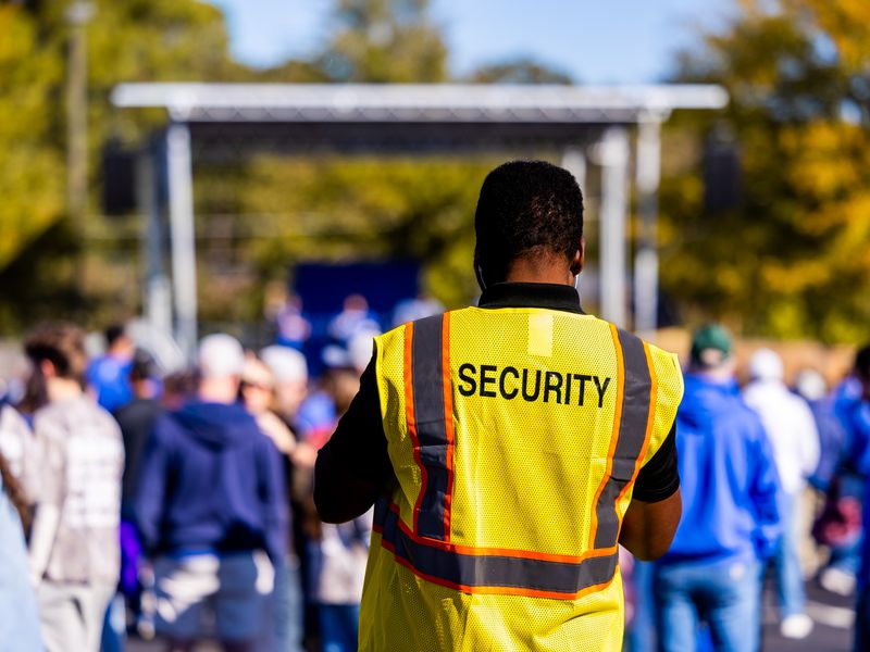 Event security steward in a yellow vest watching over an outdoor crowd