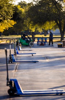 Pallet jacks and forklift in an outdoor industrial setting with trees and sunlight.