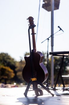 An acoustic guitar on an outdoor stage under bright sunlight, ready for a performance.