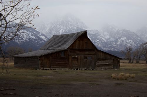 Free Wooden barn set against mountain range in Wyoming, USA, under overcast sky. Stock Photo