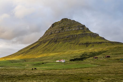 Scenic view of Kirkjufell mountain with rural houses and horses in Iceland.