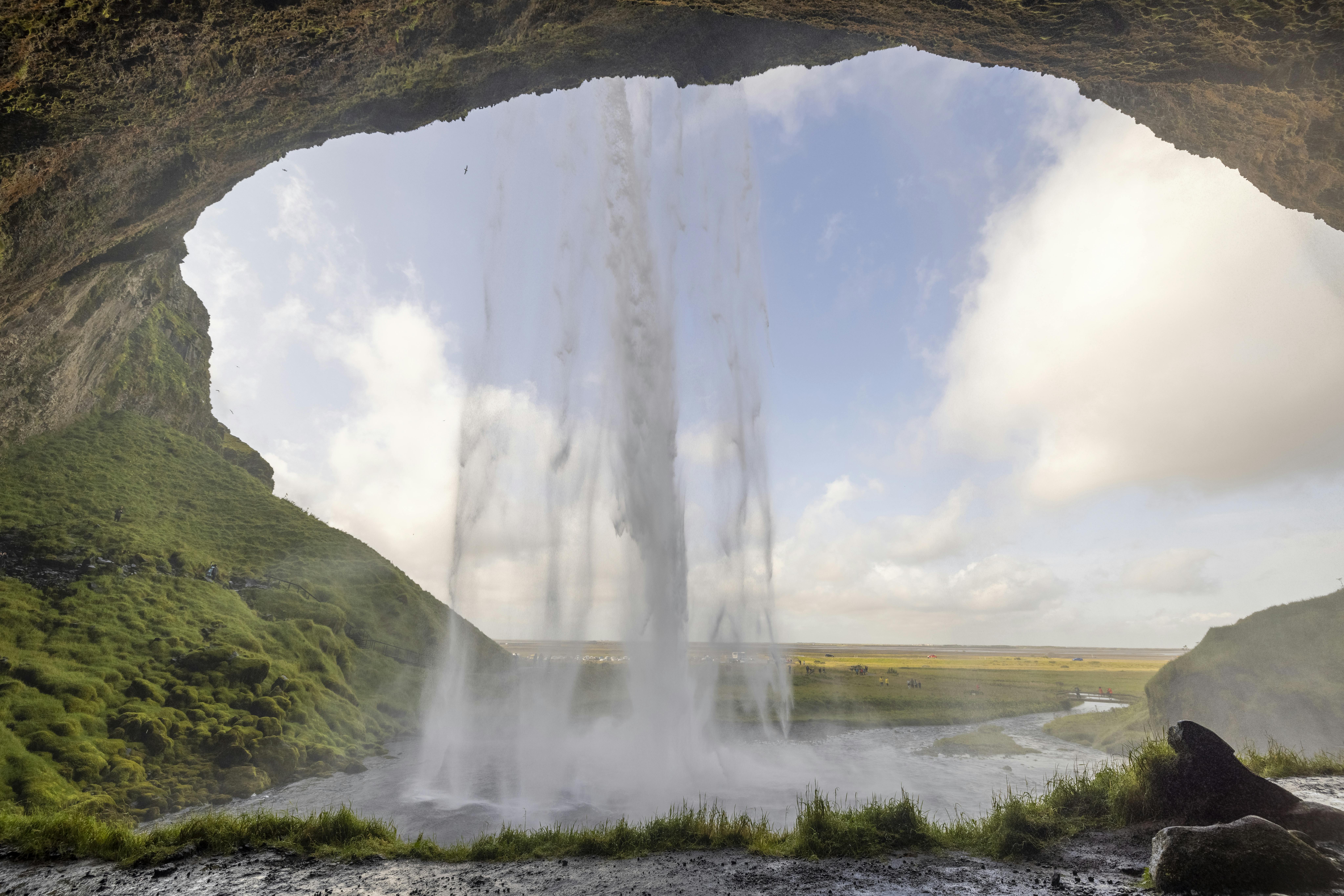 Seljalandsfoss Waterfall With A Path Behind It, Lush Green Surroundings In Summer, And Icy Conditions In Winter