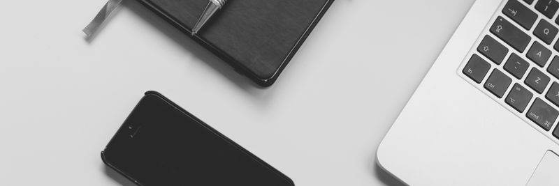 Black notebook with pen, smartphone, and laptop on a clean white desk. Perfect for business and tech themes.
