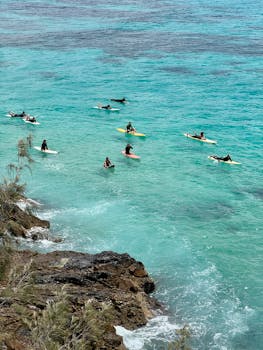 A vibrant scene of surfers on clear turquoise waters near rocky shores in Byron Bay, Australia.