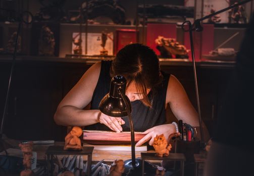 Focused artisan intricately engraving wood by lamp light, showcasing traditional craftsmanship in a cozy workshop.