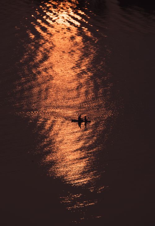 Free Silhouette of kayakers on water with golden sunset reflection for a serene and adventurous vibe. Stock Photo
