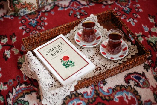 A woven tray on a patterned rug holds Turkish tea glasses and a book titled 'Şemâil-i Şerîf'.