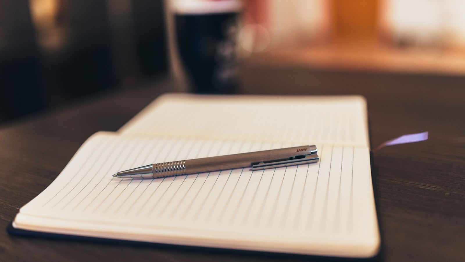 A pen resting on an open notebook with a cup in the background