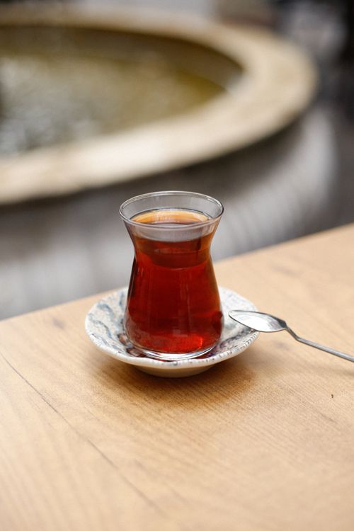 Free A glass of Turkish tea on a wooden table near a fountain, showcasing a cultural tea experience. Stock Photo