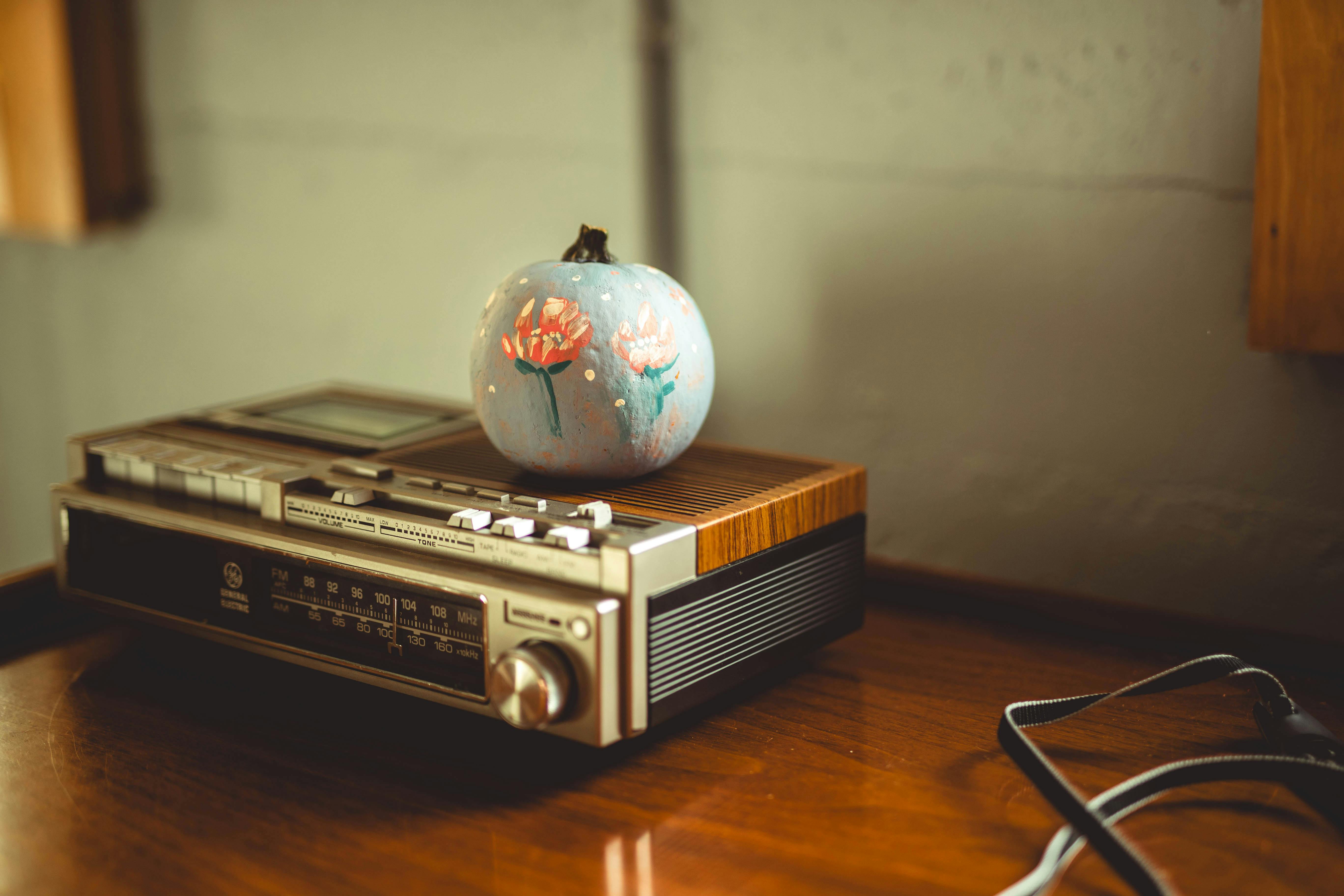 grátis Um charmoso rádio vintage adornado com uma abóbora pintada à mão, fotografado sob uma iluminação interna aconchegante. Foto profissional