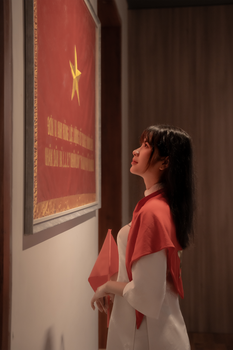 Young woman in red scarf admiring Vietnamese flag indoors.