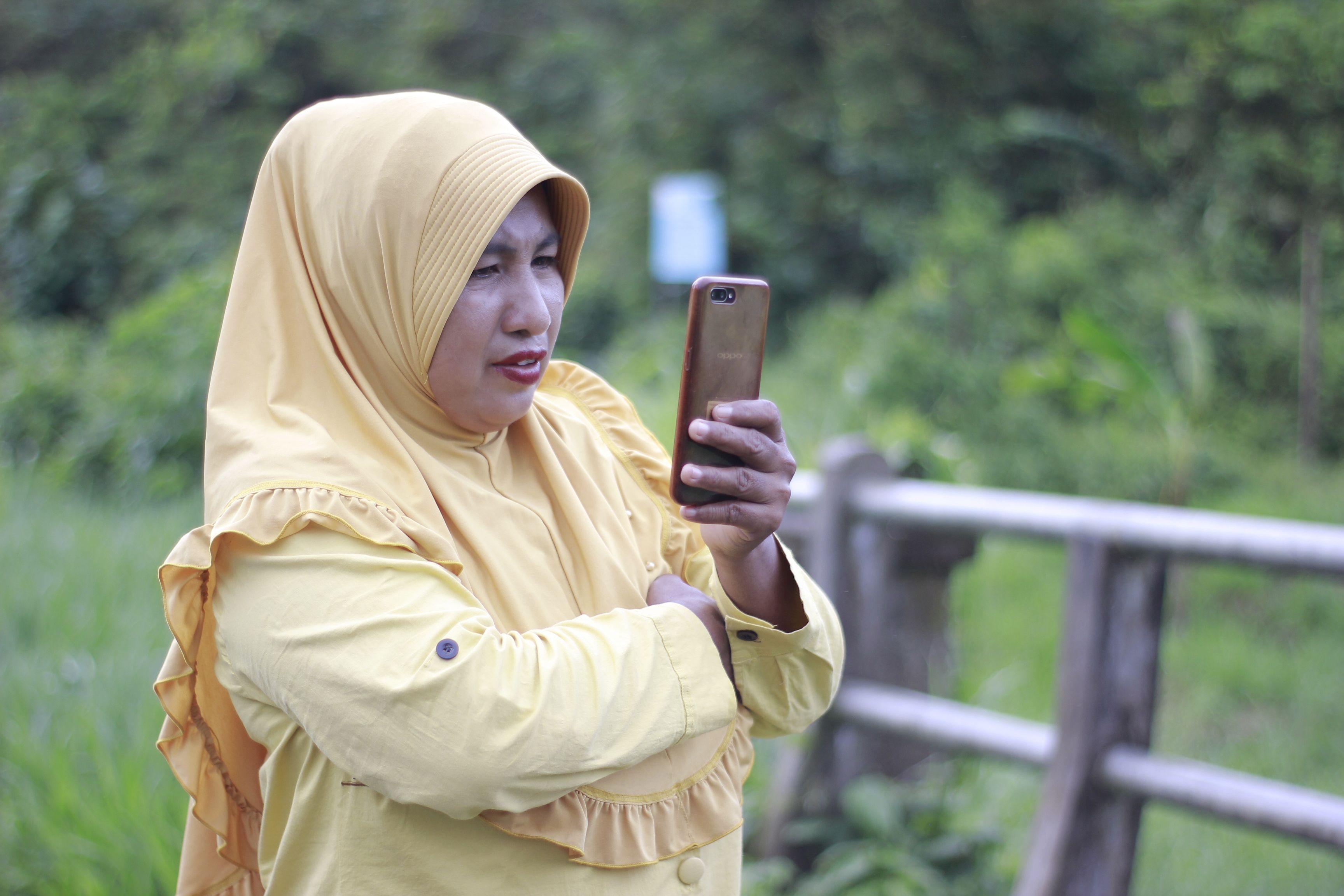 Woman in Yellow Hijab Using Smartphone Outdoors