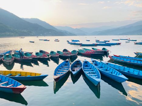 Vibrant wooden boats floating on a tranquil Nepalese lake at sunrise with mountain backdrop.