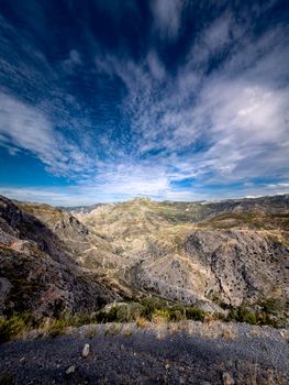 Vast and stunning rocky mountain landscape under a vibrant blue sky with scattered clouds.