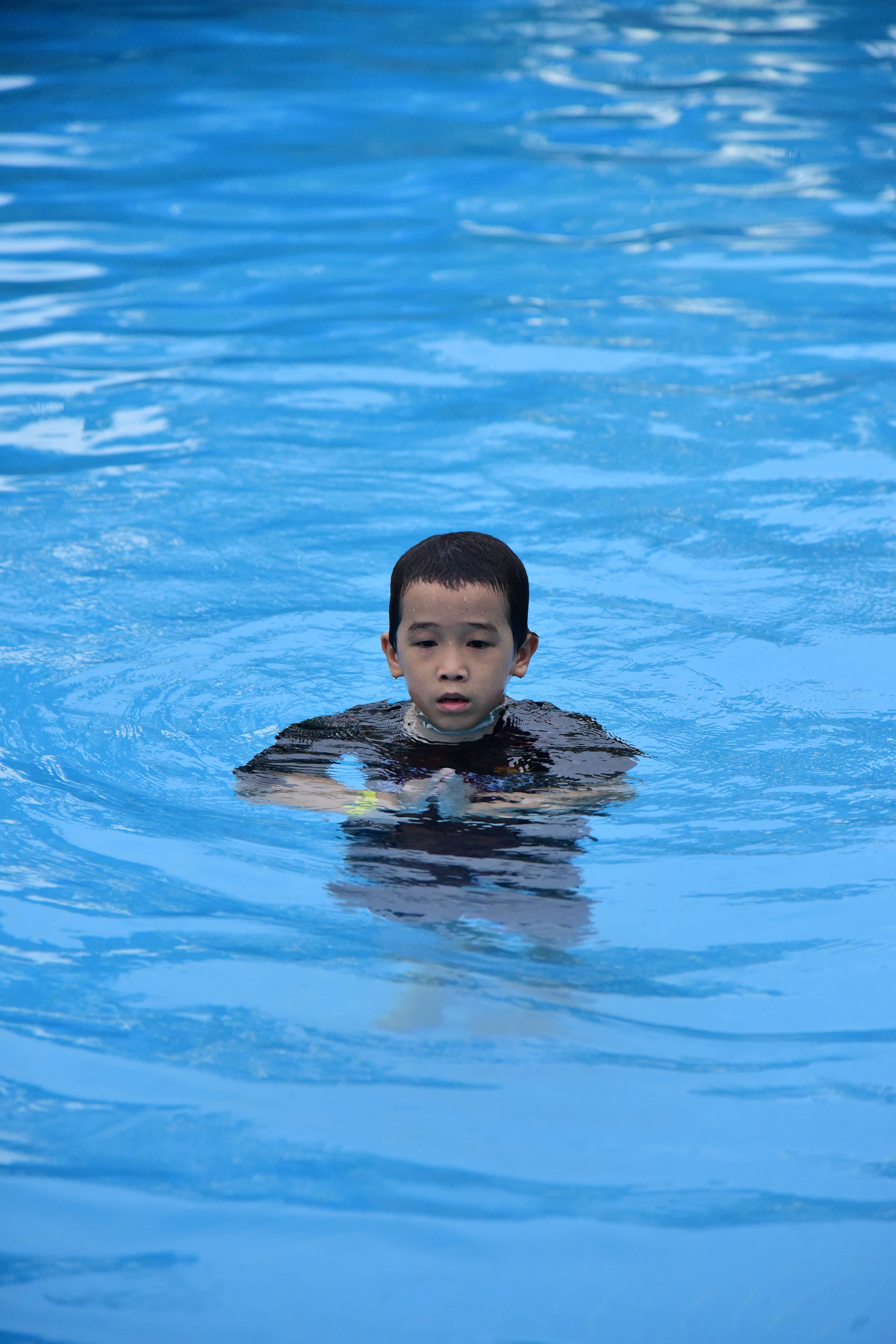 A young boy enjoying his time swimming in a clear outdoor pool.