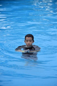 A young boy enjoying his time swimming in a clear outdoor pool.