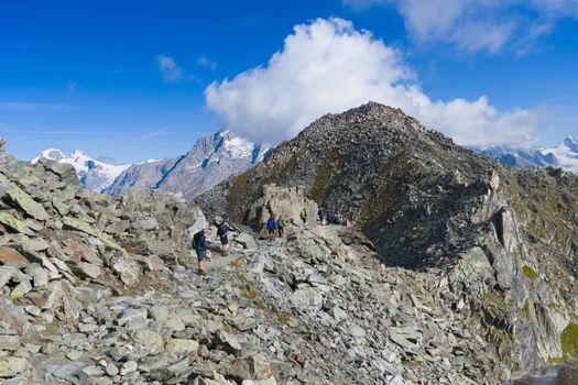 Explore the breathtaking Swiss Alps with hikers on a rocky trail under clear blue skies.