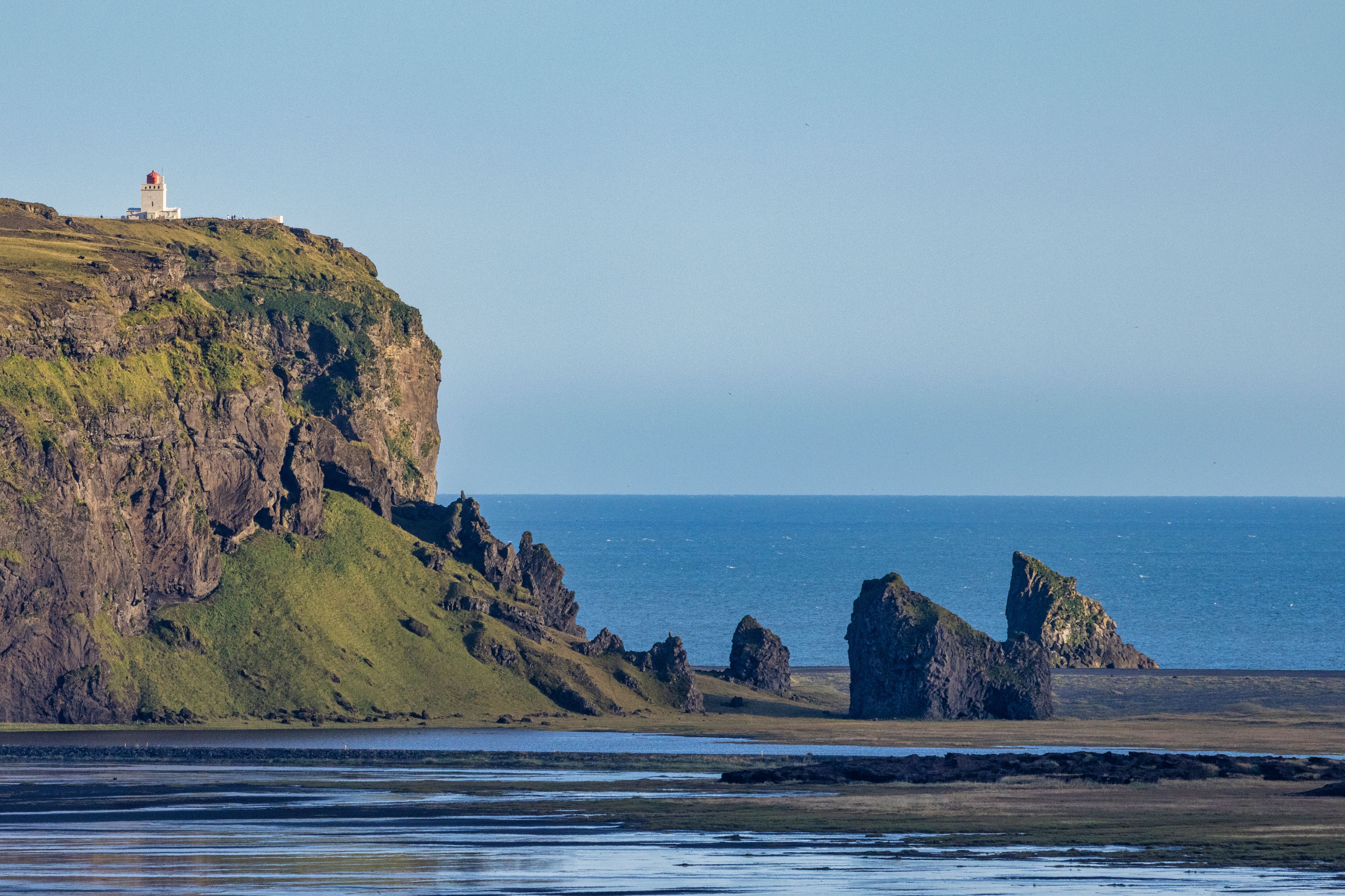 Breathtaking view of Icelandic coastline featuring a cliff, lighthouse, and ocean under clear skies.