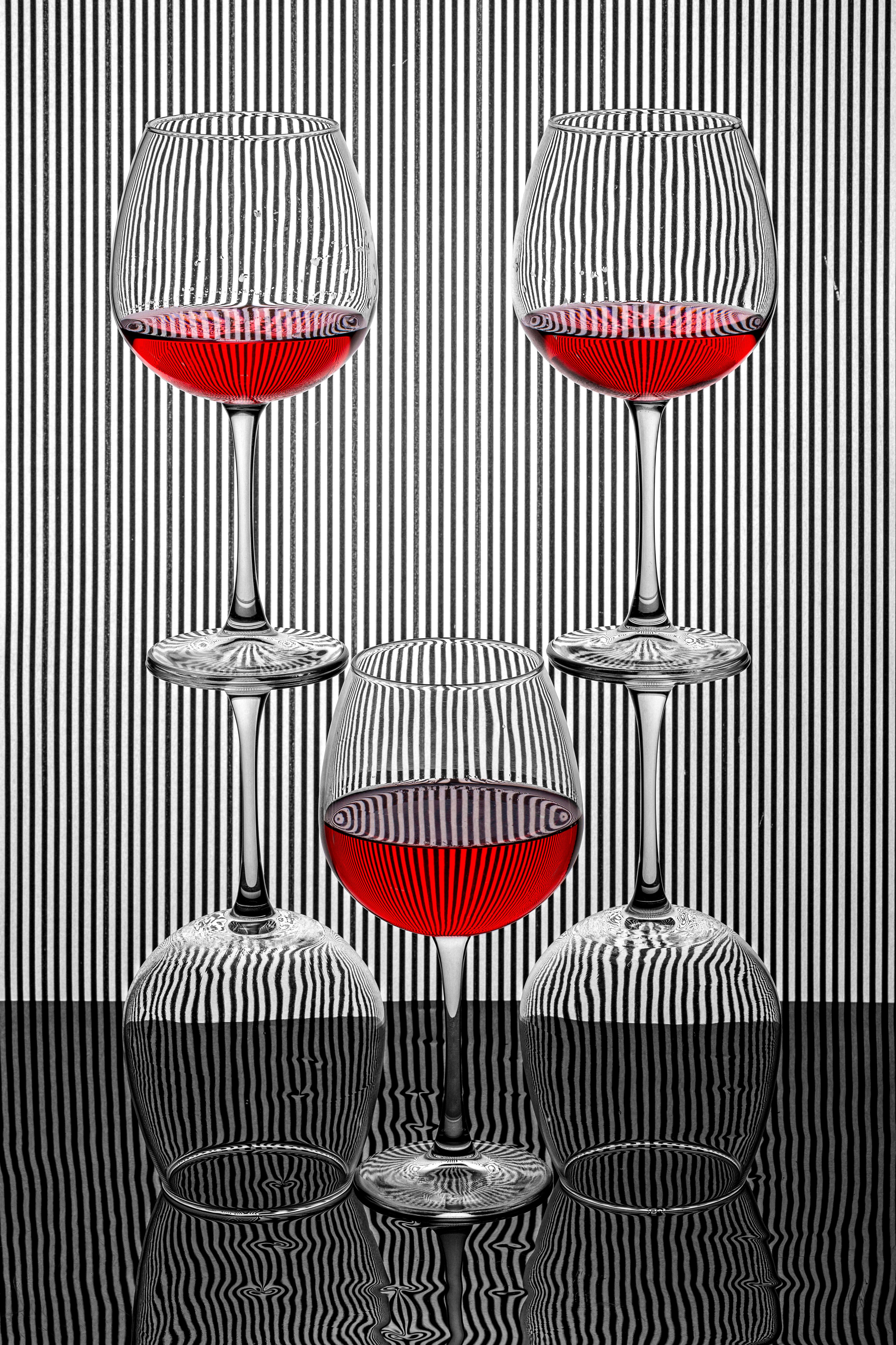 Artistic arrangement of wine glasses with red liquid and striped background, creating an abstract effect.