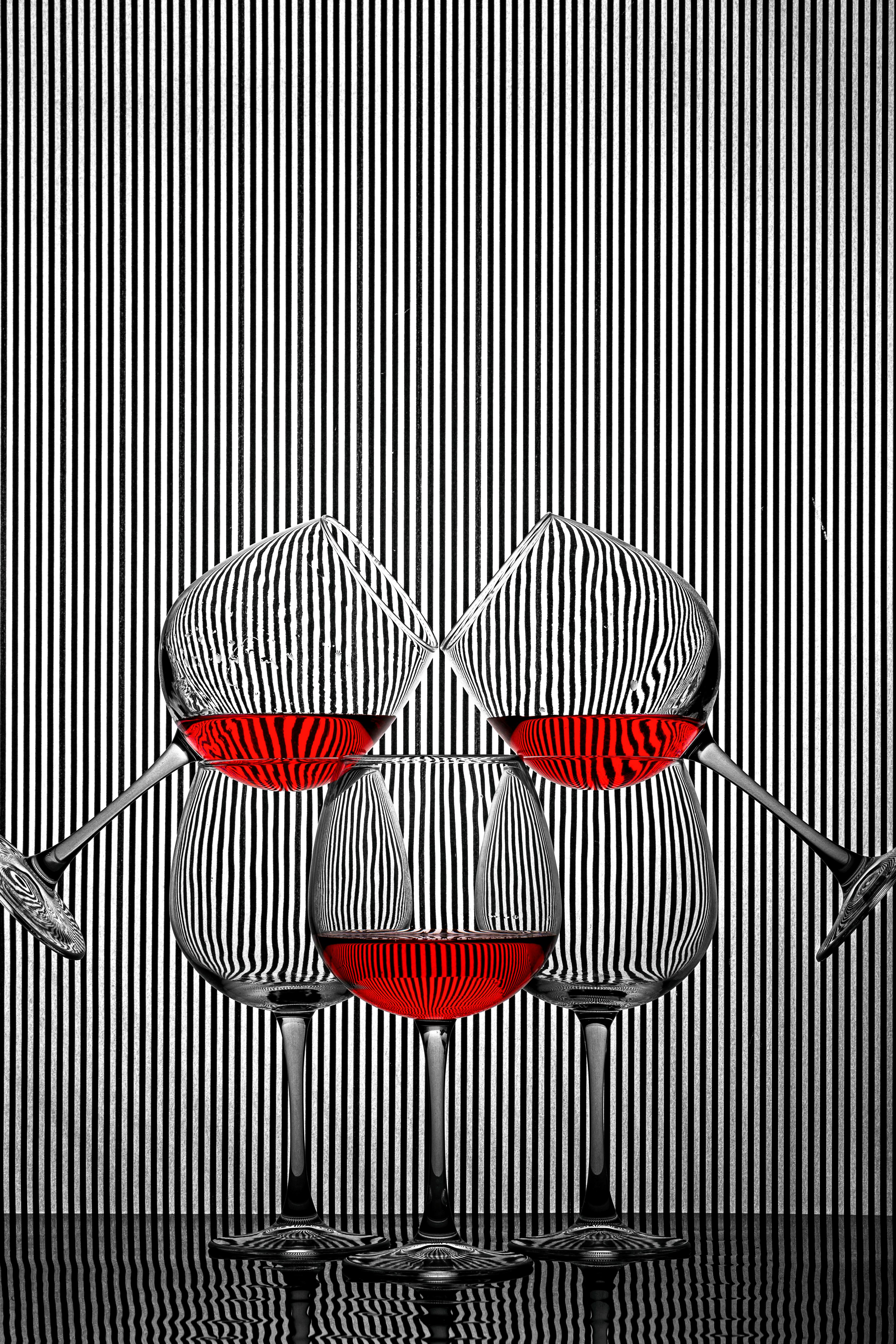 Free Three artistic wine glasses filled with red liquid, set against a striped backdrop creating an abstract visual effect. Stock Photo