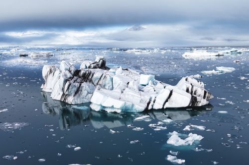 Free Stunning view of icebergs floating in cold, serene Arctic waters with a dramatic sky. Stock Photo