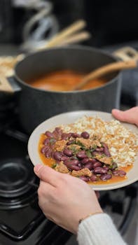 Hands serving a bean and rice dish in a kitchen setting.