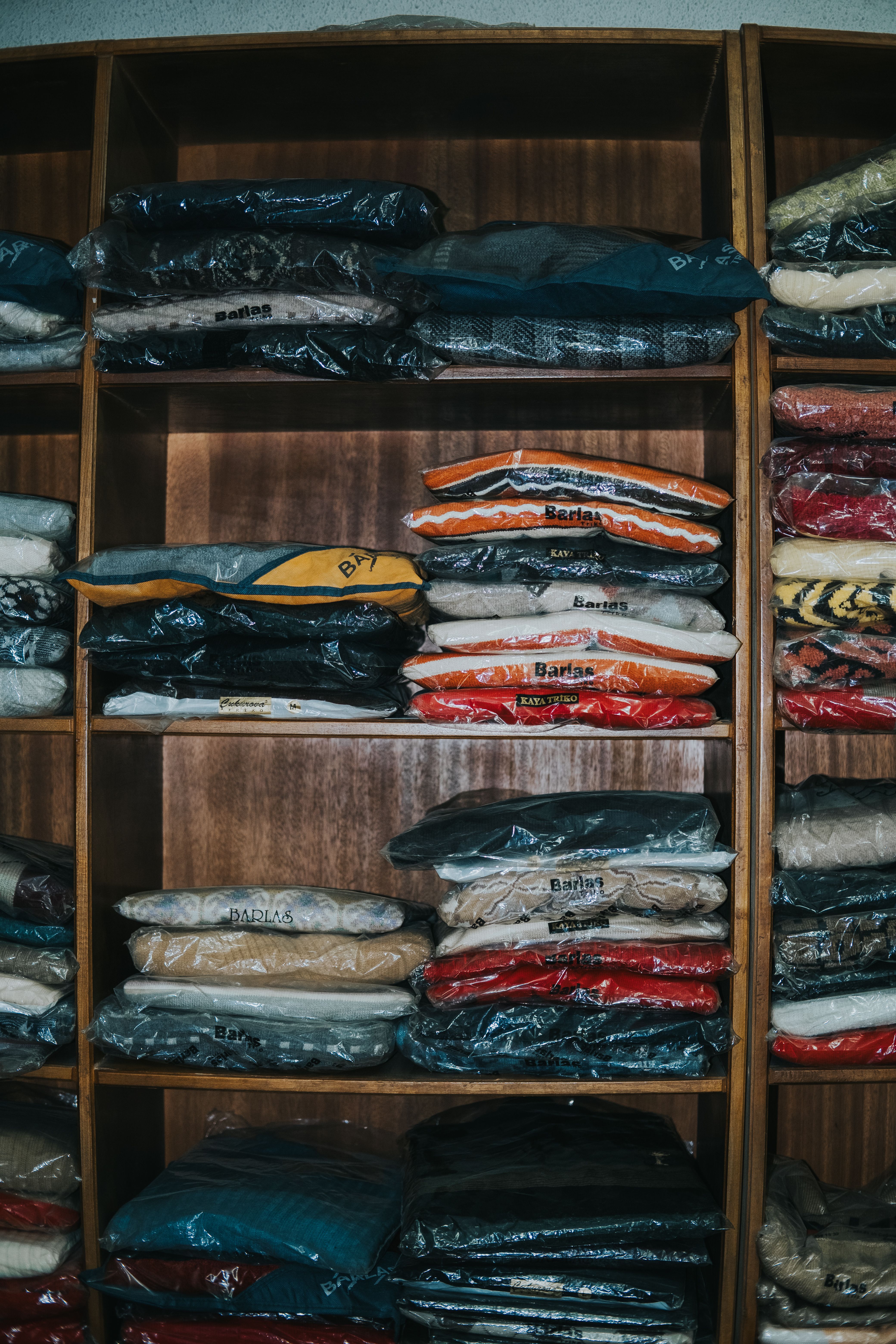 Neatly arranged clothing on shelves, each item wrapped in plastic for protection.