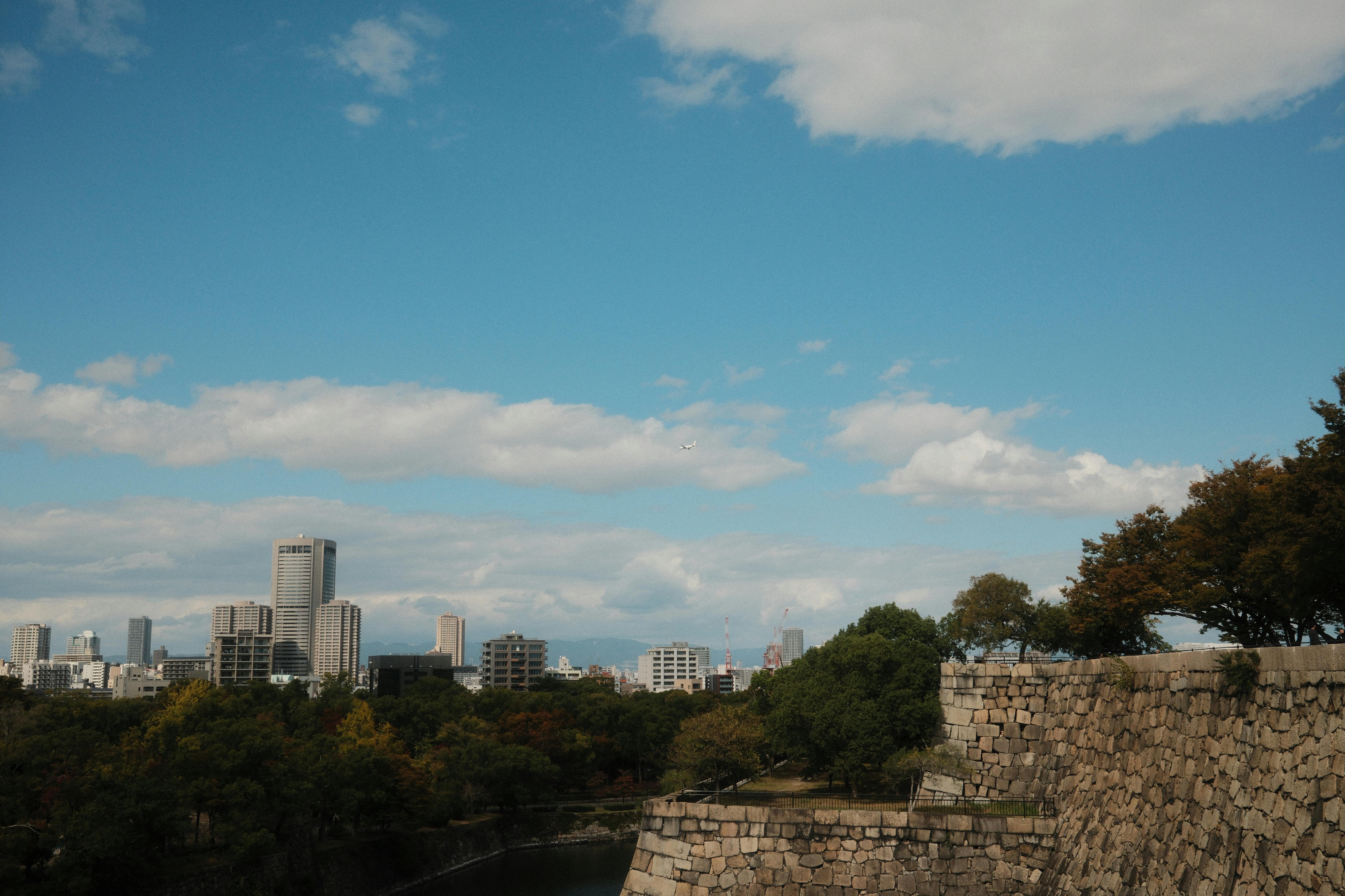 Capture of Osaka's skyline with historic castle walls and lush greenery under a bright blue sky.