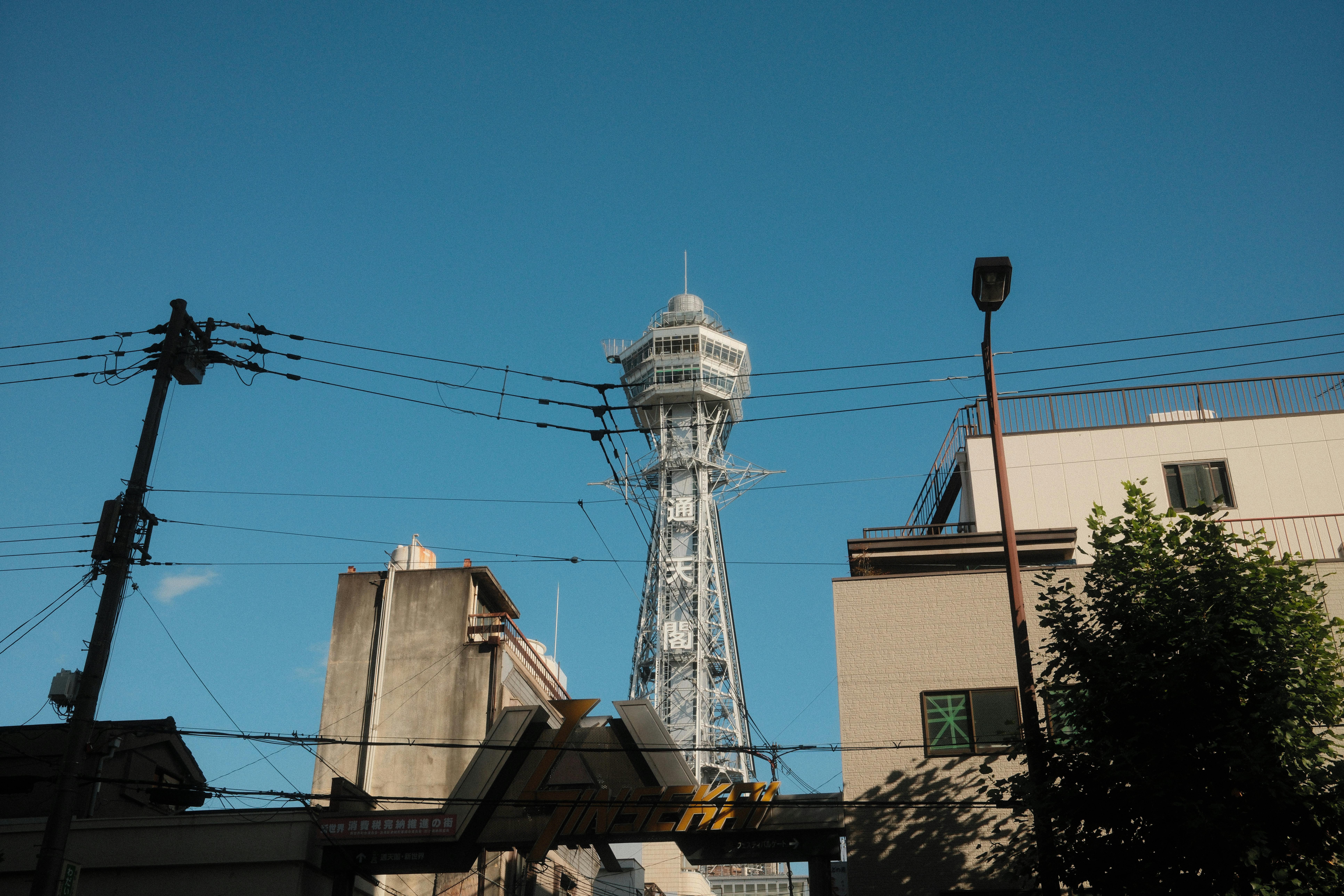 View of the Tsutenkaku Tower in Osaka, Japan, under a clear blue sky, showcasing urban architecture.