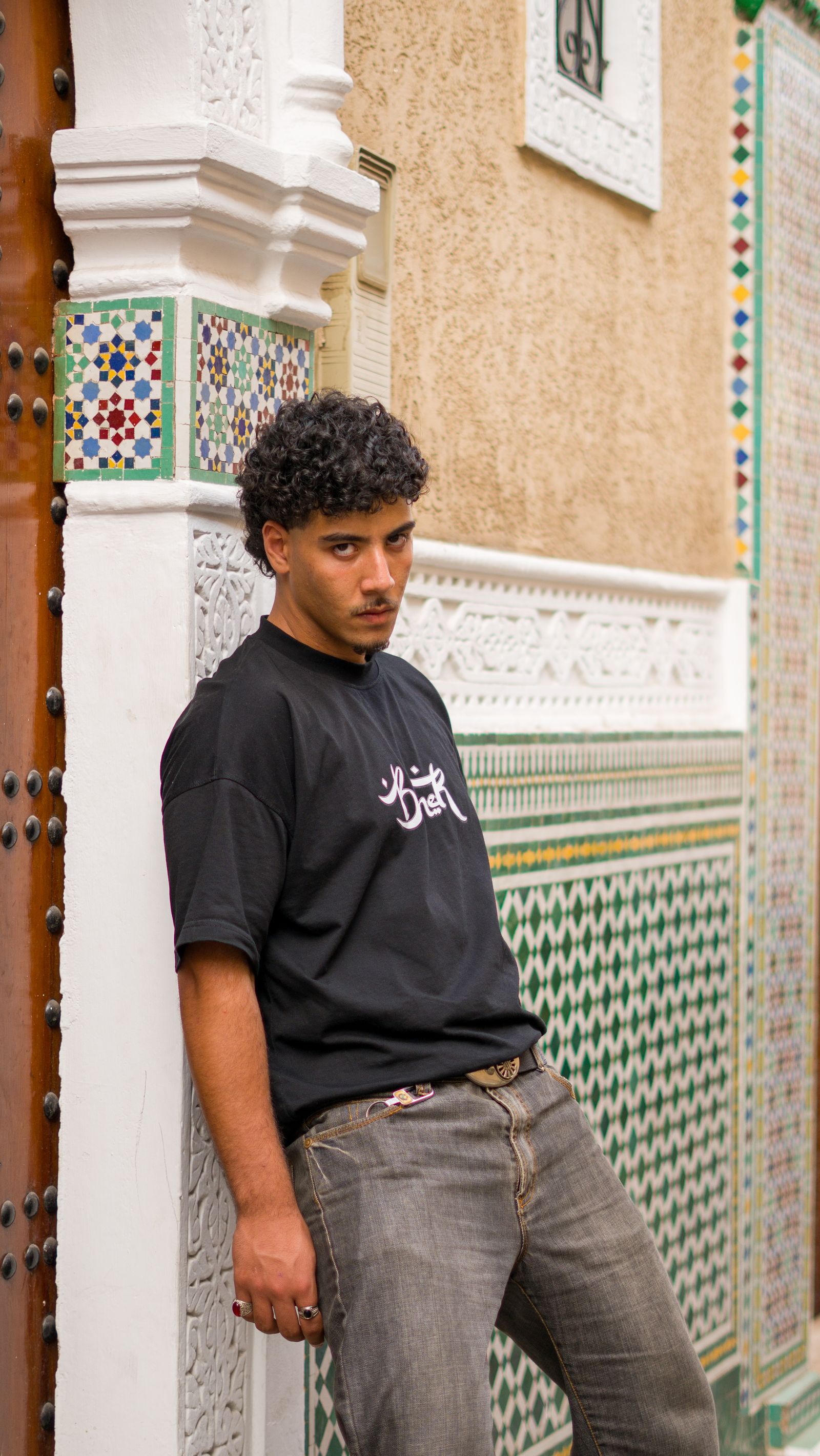 A young man in a black T-shirt beside a tiled wall and carved doorway in Morocco