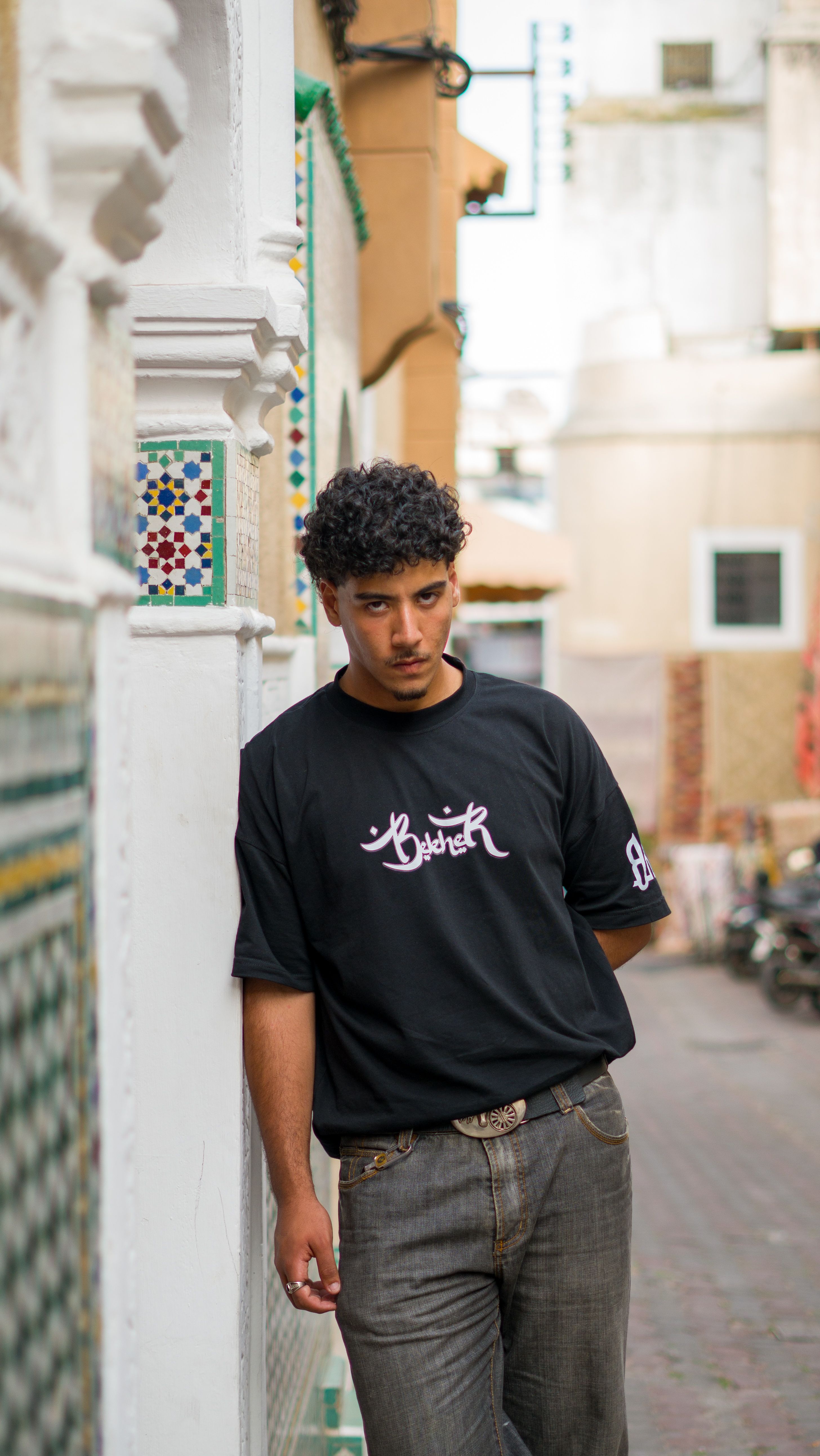 Casual portrait of a young man leaning against a wall in a Moroccan street, captured in daylight.