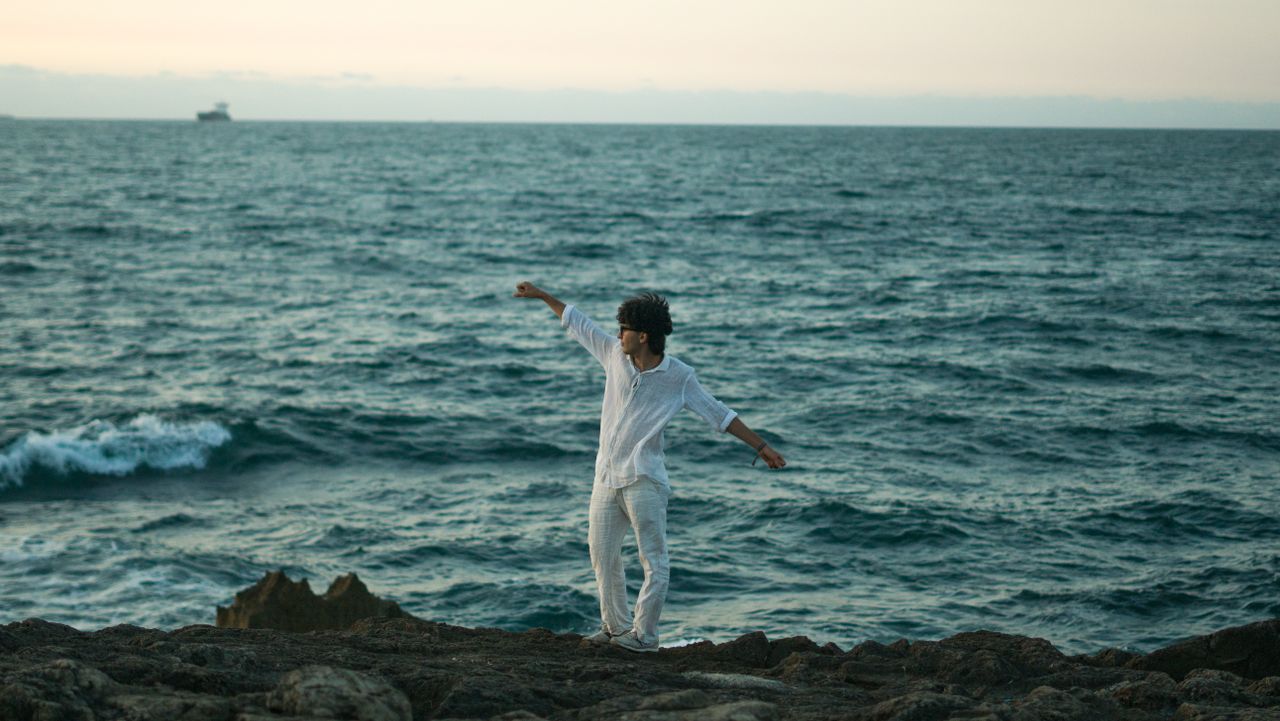 a person in white clothes joyfully dancing on a rocky coast with the o