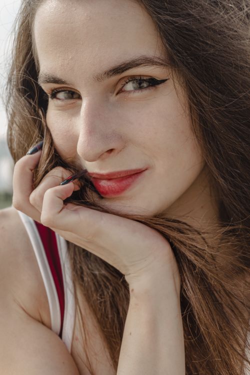 Free A close-up portrait of a smiling woman with red lipstick and long hair outdoors. Stock Photo