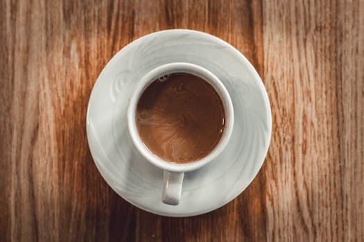Aerial shot of a cup of coffee in a white saucer placed on a wooden table, emphasizing simplicity and warmth.