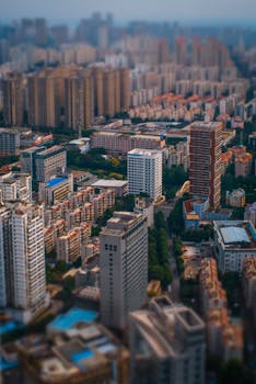Tilt-shift aerial view of a bustling city with various buildings and green spaces.