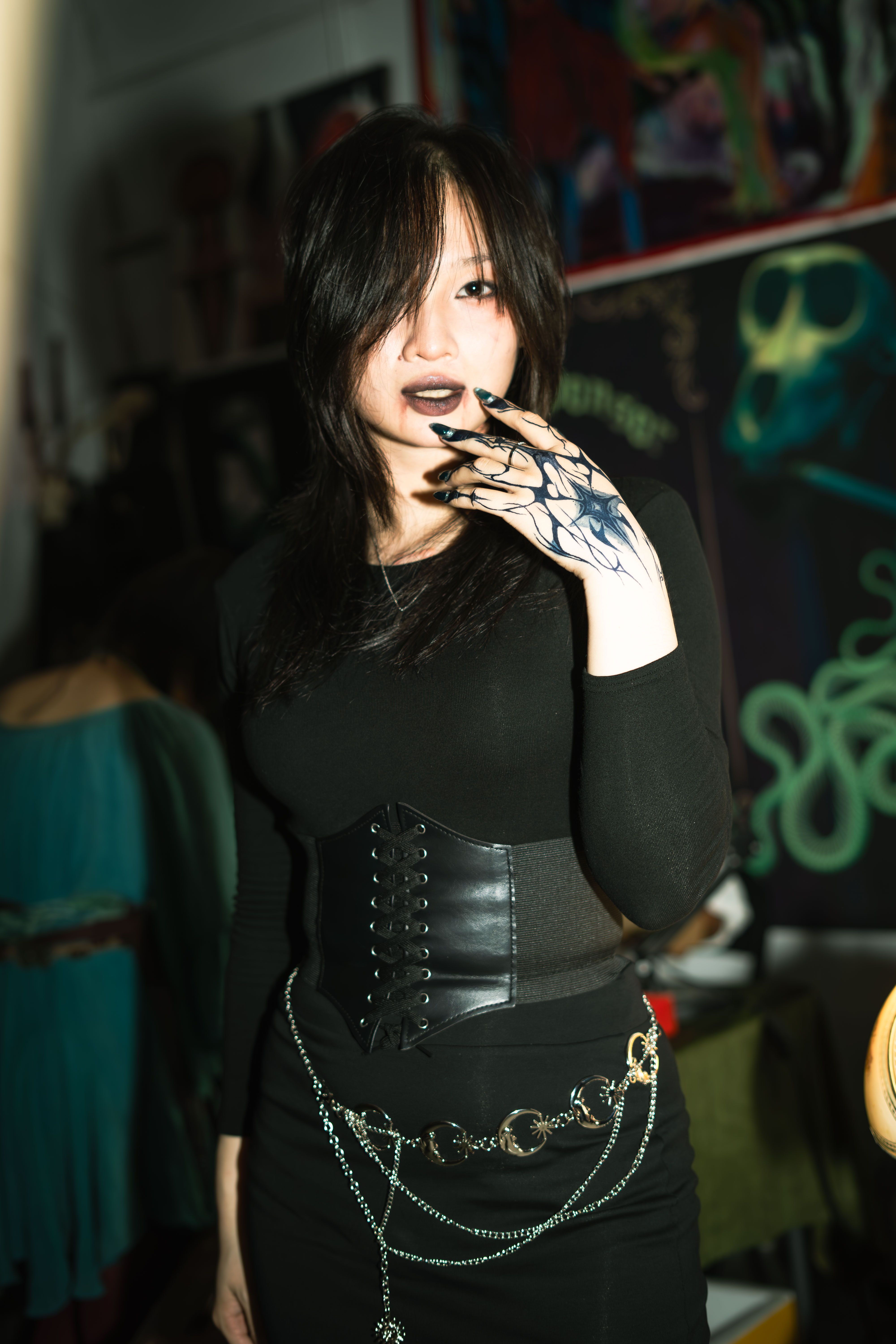 Portrait of a fashionable woman in goth style with tattooed hand and dark attire, indoors.