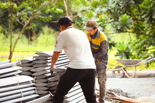 Free Two male workers organize metal sheets at a construction site surrounded by greenery. Stock Photo
