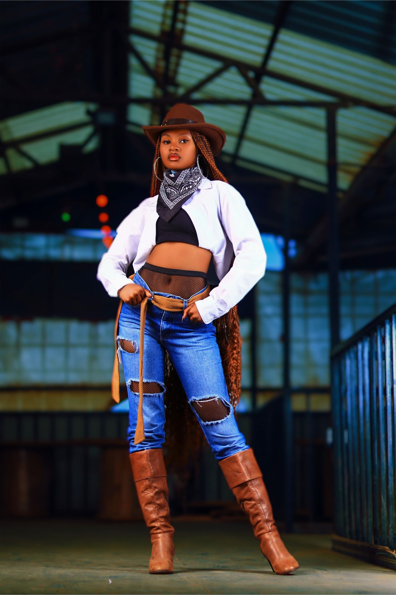 Woman in a country concert outfit with a cowboy hat, bandana, ripped jeans and tall brown boots