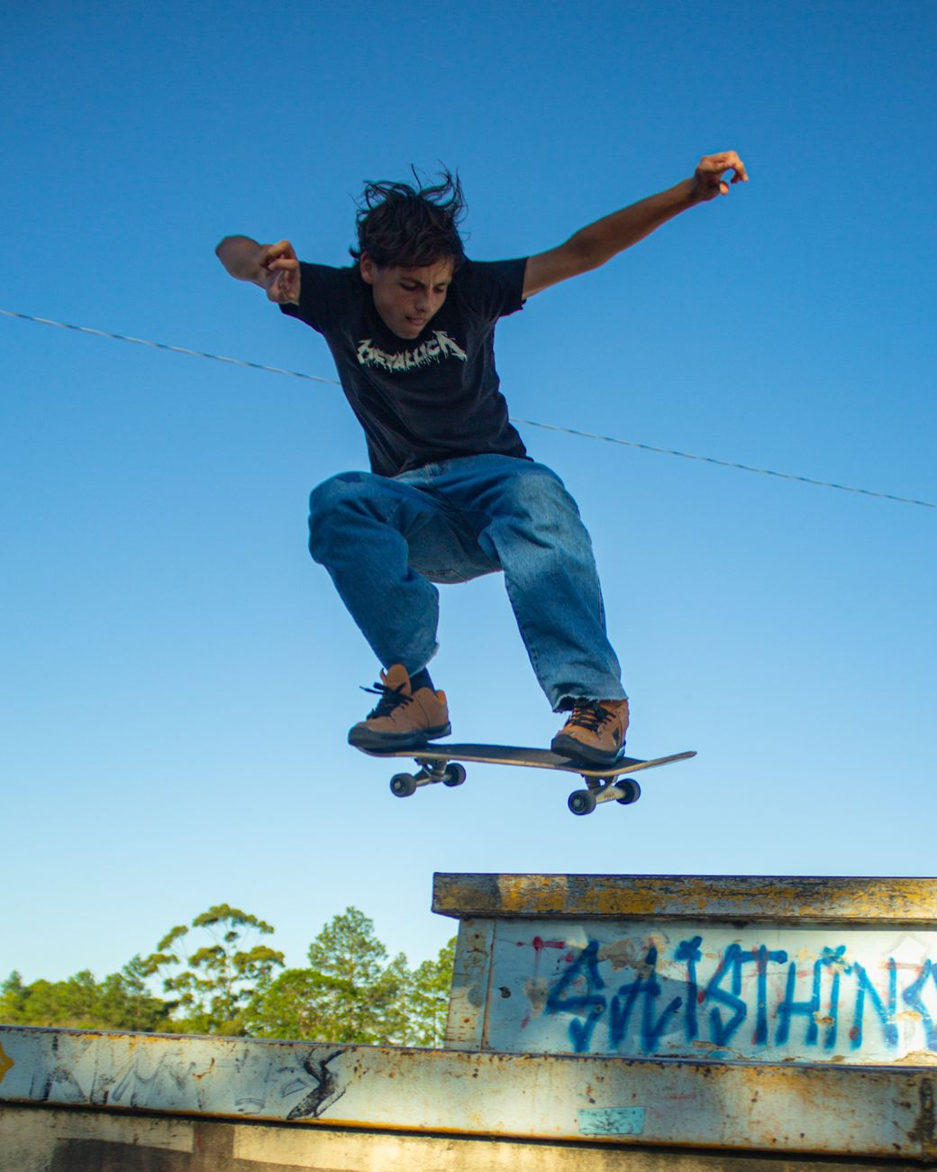 A teenager performs a skateboarding trick mid-air against a clear blue sky.. teenager, performs, skateboarding